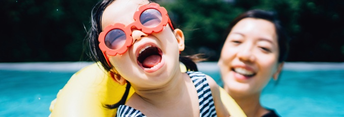 Points with Flybuys Travel Child wearing red flower sunglasses and yellow floaty toy held by smiling mother in swimming pool
