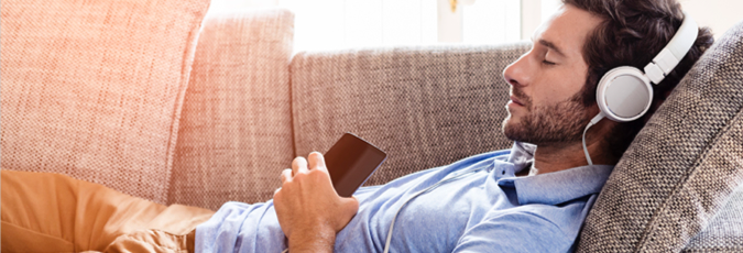 Guy laying on the couch with his eyes closed listening to his music via headphones