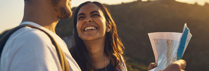 Happy couple looking at a map while hiking at sunset