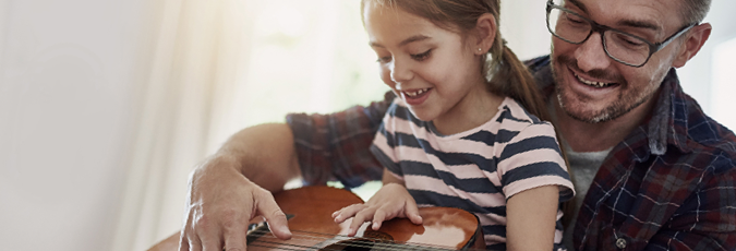 Dad with his daughter on his lap teaching her the guitar