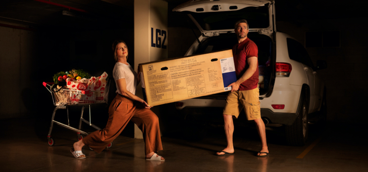 A young couple attempting to put a flat pack box into the boot of the car