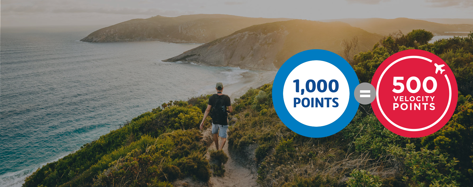 Man in a baseball cap and blue shorts hiking along a grassy path overlooking the coastline