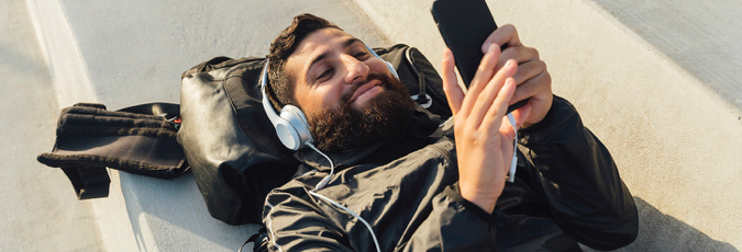 Access Optus' 5G Network at no extra cost Young man with a beard and headphones lying on the ground on his phone