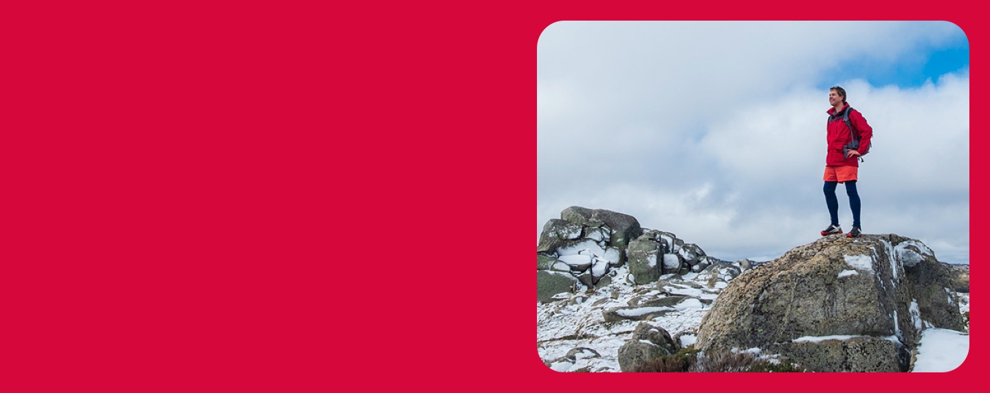 Young man in hiking gear standing on the top of a mountain with the sky in the background