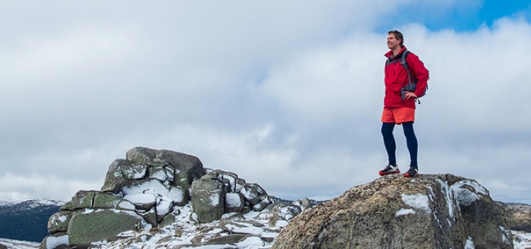Young man in hiking gear standing on the top of a mountain with the sky in the background