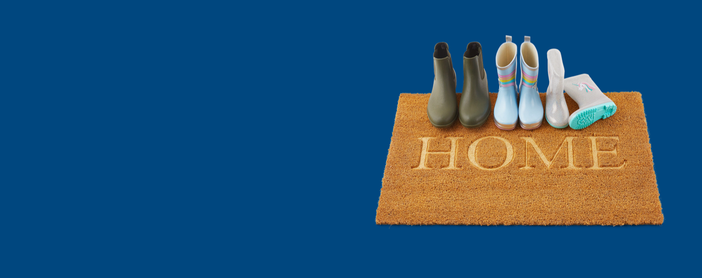 Three pairs of gumboots sitting on a coir door mat 