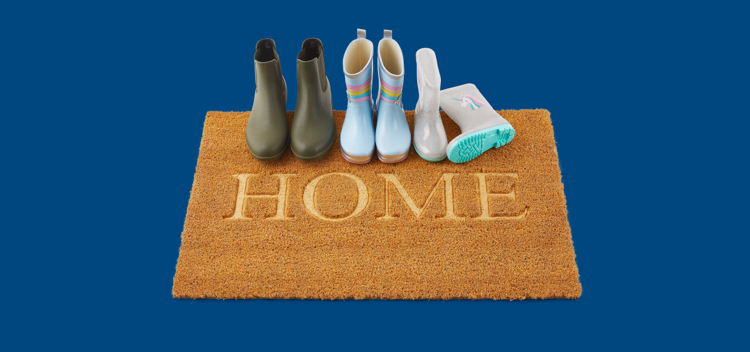 Three pairs of gumboots sitting on a coir door mat