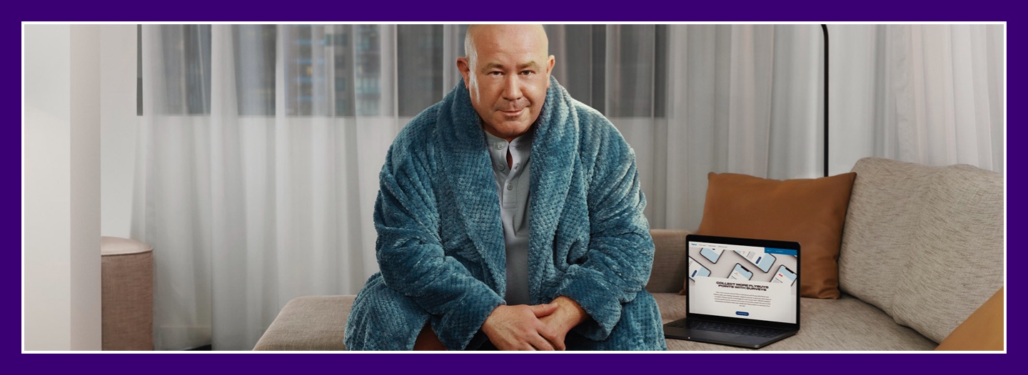 Flybuys' top 10 member Dale sitting on couch in his bathrobe next to laptop showing Flybuys' app web page