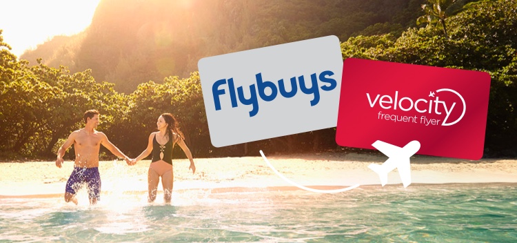 Couple holding hands knee deep in water with a Flybuys and Velocity Frequent Flyer card above their heads