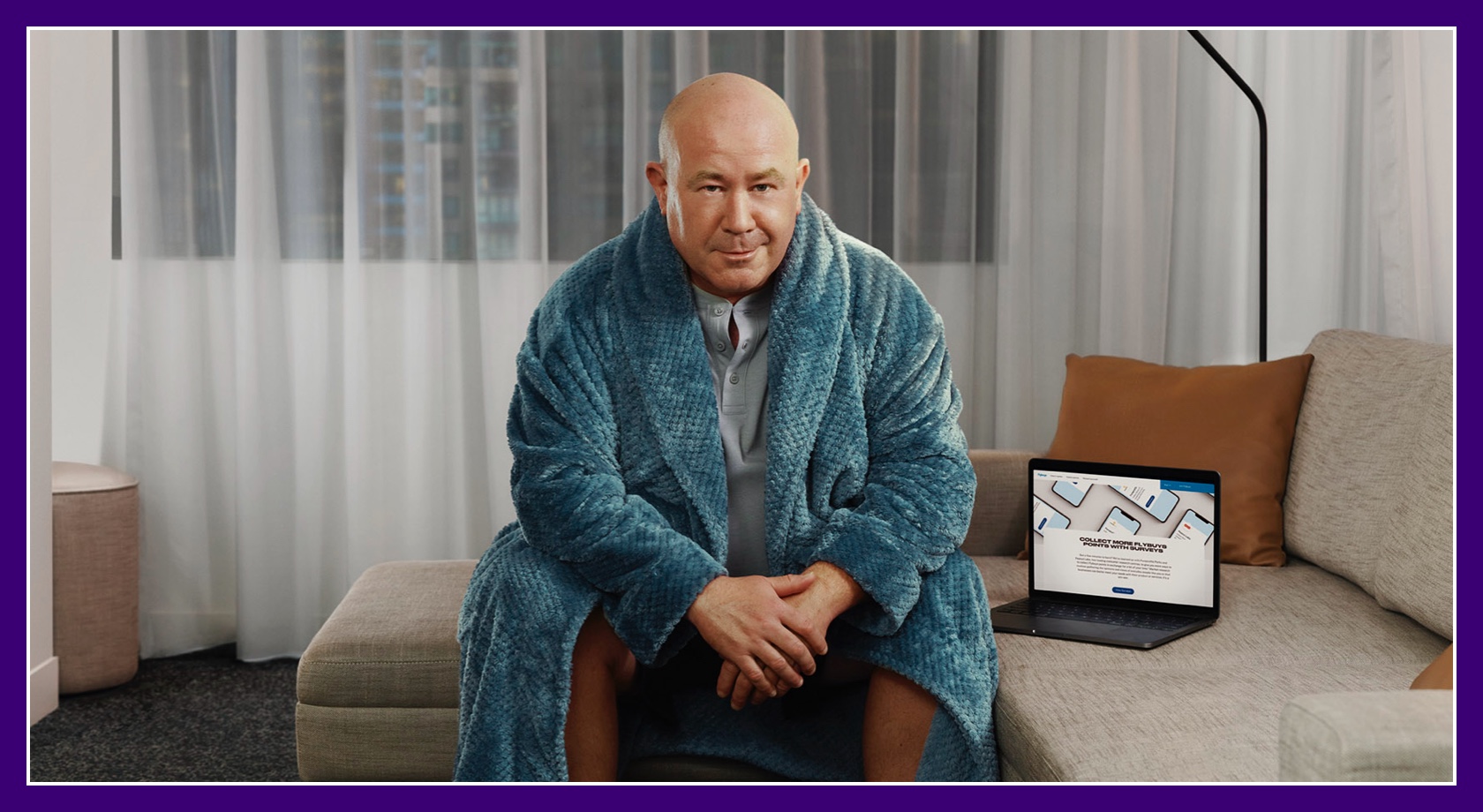 Flybuys' top 10 member Dale sitting on couch in his bathrobe next to laptop showing Flybuys' app web page