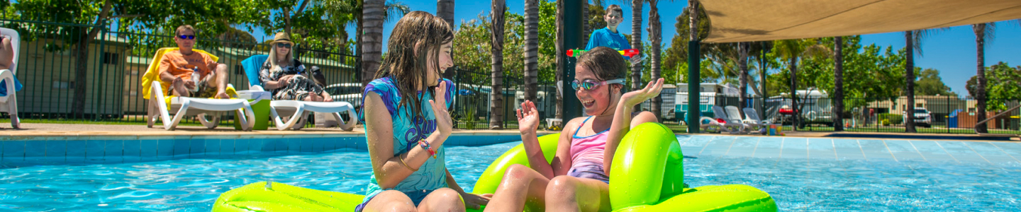 Children playing in the pool while family sunbathes
